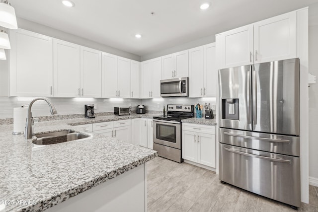 kitchen featuring appliances with stainless steel finishes, pendant lighting, sink, white cabinets, and light stone counters