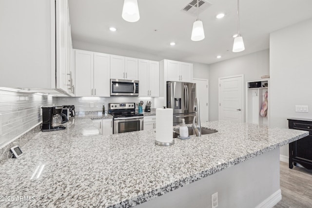 kitchen with white cabinetry, hanging light fixtures, stainless steel appliances, light stone counters, and kitchen peninsula