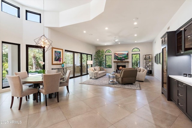 dining room featuring recessed lighting, a warm lit fireplace, light tile patterned flooring, and ceiling fan with notable chandelier