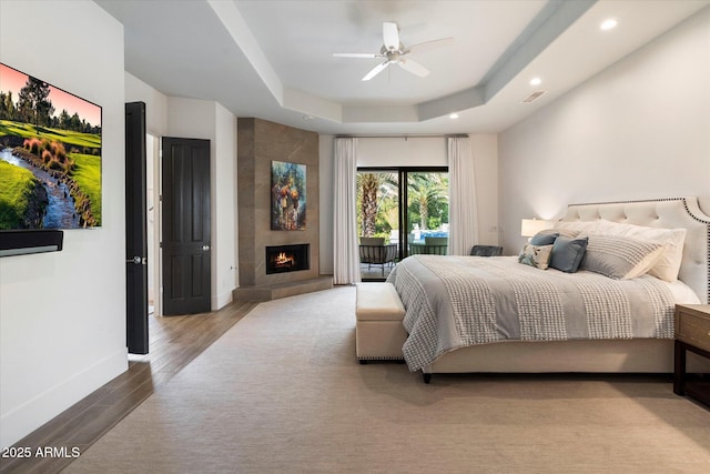 bedroom with visible vents, a tray ceiling, wood finished floors, baseboards, and access to exterior