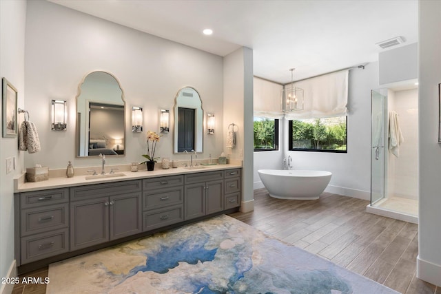 bathroom with wood finished floors, visible vents, double vanity, a freestanding bath, and a sink