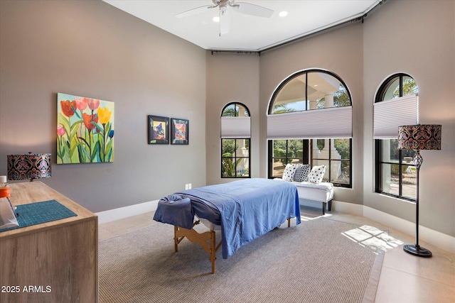 bedroom featuring a ceiling fan, a high ceiling, and baseboards