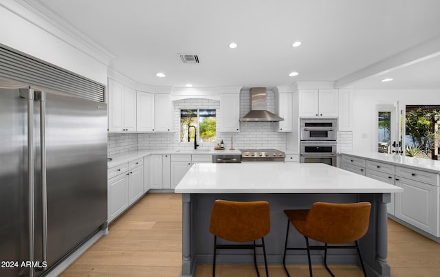 kitchen with white cabinets, a center island, stainless steel appliances, and wall chimney exhaust hood