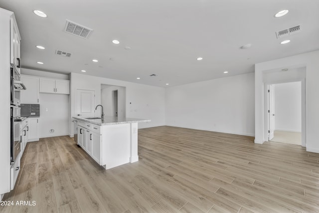 kitchen with sink, a kitchen island with sink, white cabinetry, light stone countertops, and light hardwood / wood-style floors