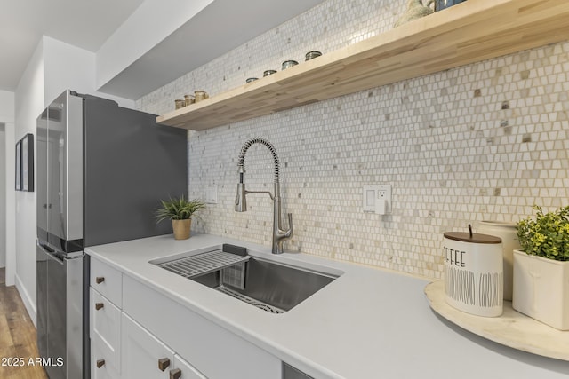 kitchen with stainless steel refrigerator, wood-type flooring, sink, white cabinets, and decorative backsplash