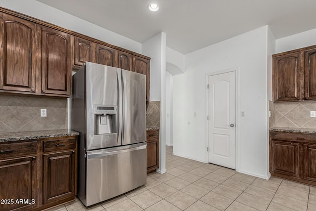 28232 N Abby Cir, San Tan Valley, AZ 85143 - kitchen with stainless steel fridge with ice dispenser, light tile patterned floors, dark stone counters, arched walkways, and dark brown cabinetry