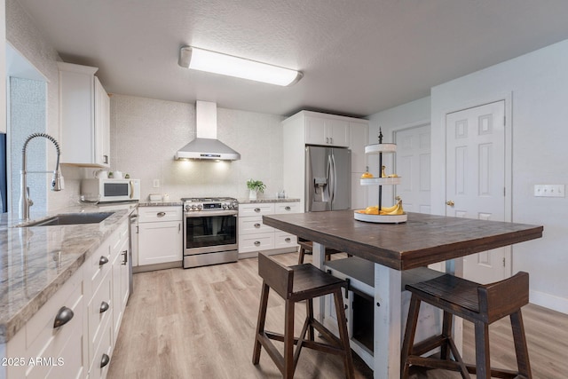 21188 N Duncan Dr, Maricopa, AZ 85138 - kitchen with wall chimney range hood, stainless steel appliances, a sink, light wood finished floors, and white cabinetry