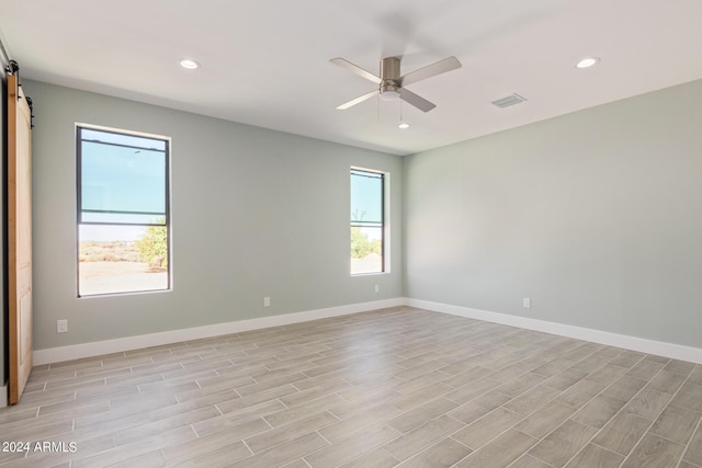 spare room with ceiling fan, a barn door, and light wood-type flooring