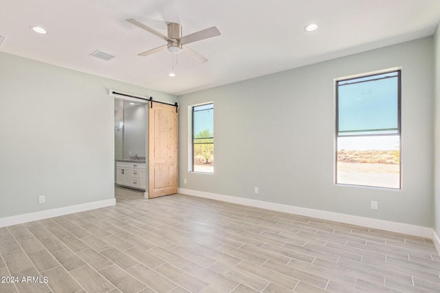 unfurnished bedroom with ceiling fan, connected bathroom, a barn door, and light wood-type flooring