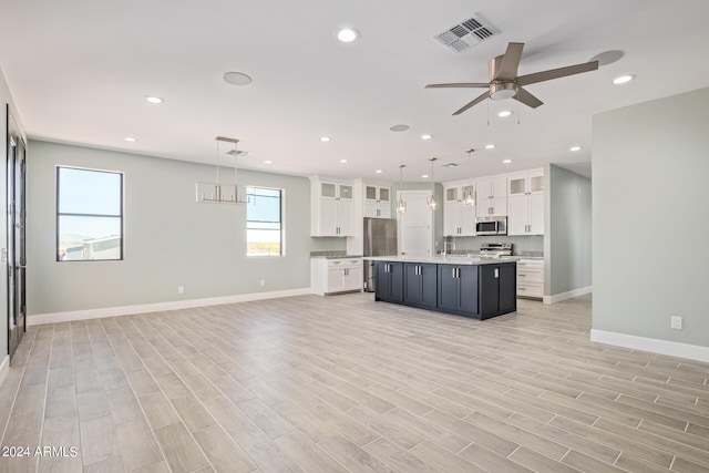 kitchen featuring an island with sink, appliances with stainless steel finishes, white cabinets, and decorative light fixtures