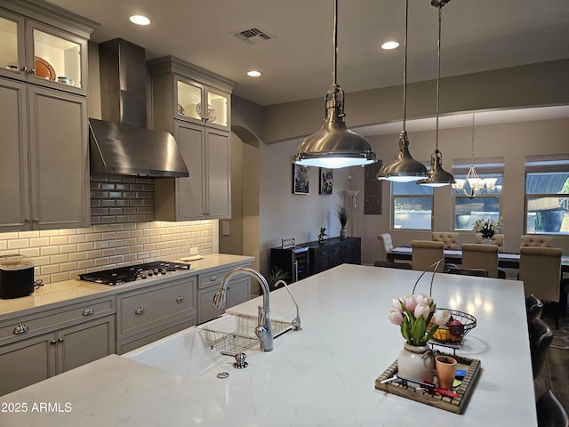 kitchen with stainless steel gas cooktop, light countertops, visible vents, decorative backsplash, and wall chimney exhaust hood