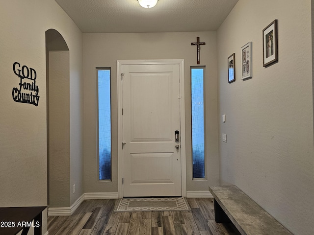 entrance foyer with arched walkways, a textured ceiling, and dark wood finished floors