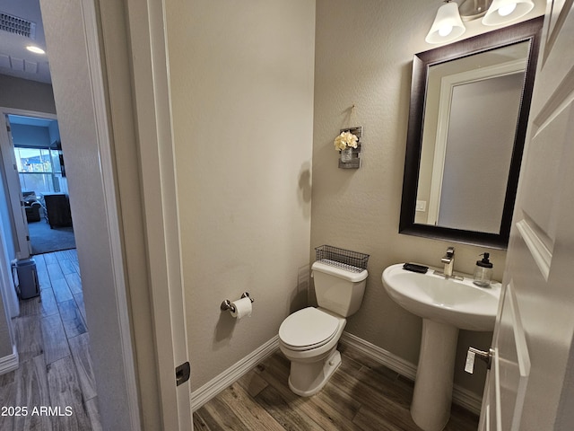 bathroom with toilet, a sink, wood finished floors, visible vents, and baseboards