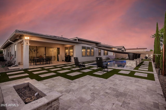 back of house at dusk with an outdoor fire pit, a fenced in pool, outdoor dining area, a patio area, and stucco siding