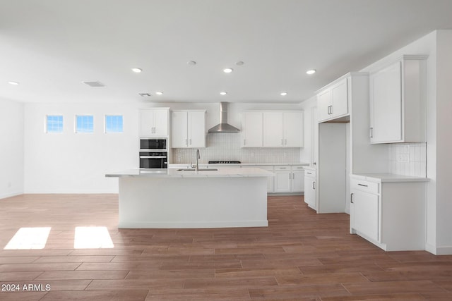 kitchen with white cabinets, sink, an island with sink, and wall chimney range hood