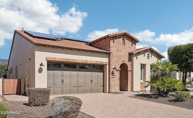 mediterranean / spanish home with brick siding, roof mounted solar panels, an attached garage, and decorative driveway