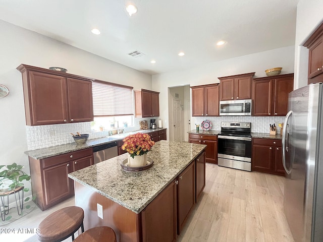 kitchen with light hardwood / wood-style floors, tasteful backsplash, a kitchen island, stainless steel appliances, and light stone countertops