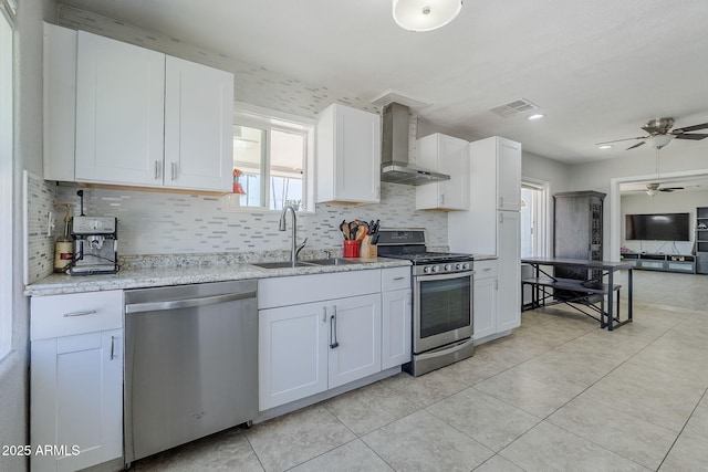 kitchen featuring visible vents, a ceiling fan, wall chimney exhaust hood, a sink, and stainless steel appliances