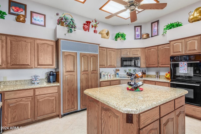 kitchen with light stone counters, black appliances, light tile patterned flooring, a kitchen island, and ceiling fan