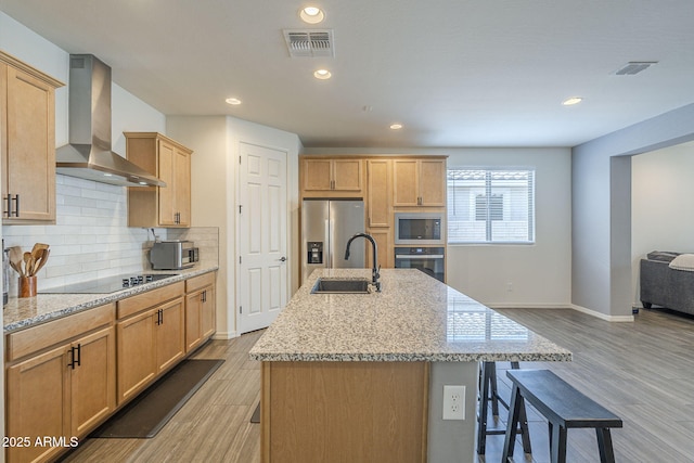 17618 W Medlock Dr, Litchfield Park, AZ 85340 - kitchen featuring wall chimney range hood, appliances with stainless steel finishes, a sink, light wood-type flooring, and a kitchen breakfast bar