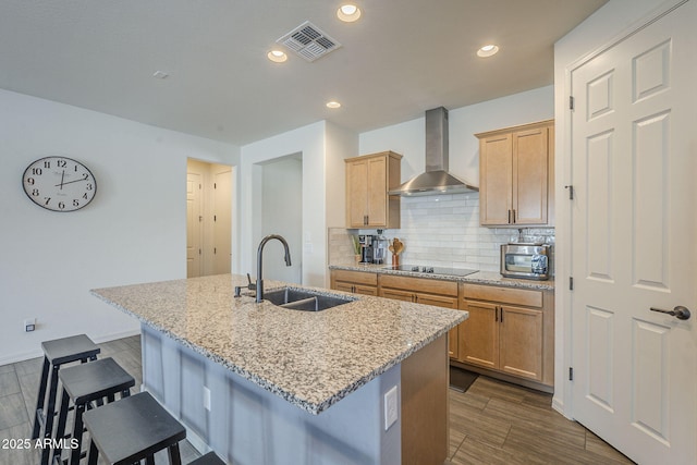 17618 W Medlock Dr, Litchfield Park, AZ 85340 - kitchen featuring wall chimney range hood, a sink, a center island with sink, a kitchen bar, and backsplash