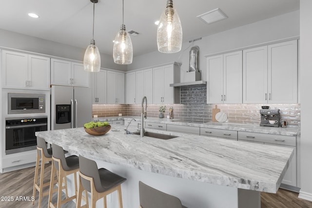 kitchen featuring white cabinets, wall chimney exhaust hood, stainless steel appliances, sink, and hanging light fixtures