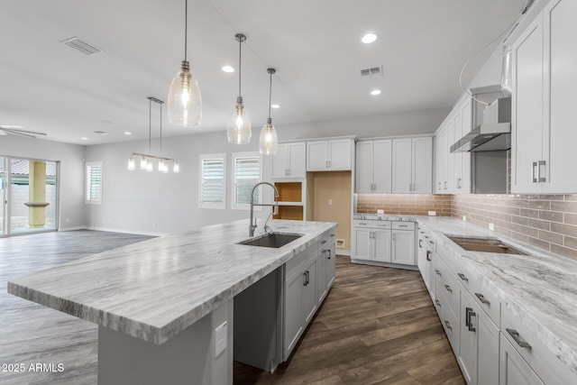 kitchen featuring light stone countertops, white cabinetry, tasteful backsplash, sink, and a kitchen island with sink