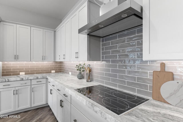 kitchen with backsplash, black electric stovetop, white cabinetry, wall chimney exhaust hood, and light stone counters