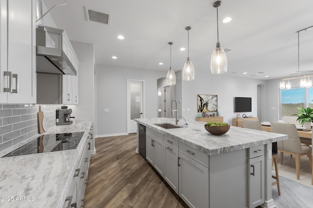 kitchen with a kitchen island with sink, sink, wall chimney range hood, pendant lighting, and black appliances