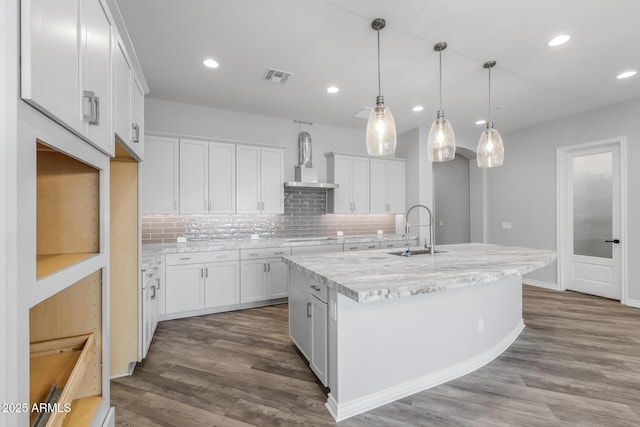 kitchen with decorative light fixtures, white cabinetry, wall chimney range hood, an island with sink, and sink