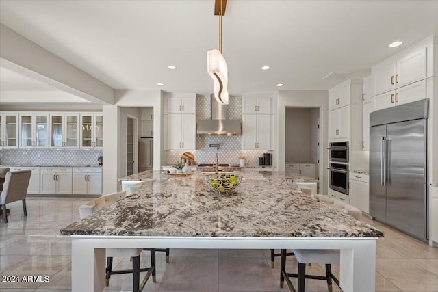 kitchen with light stone counters, stainless steel appliances, a spacious island, pendant lighting, and white cabinetry