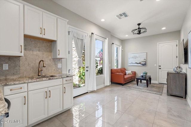 kitchen with light stone countertops, decorative backsplash, white cabinetry, and sink