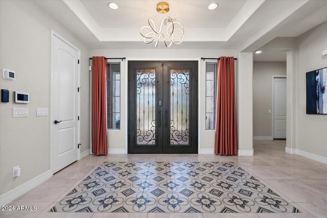 tiled foyer entrance with french doors, a tray ceiling, and a notable chandelier