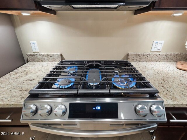 interior details featuring exhaust hood, light stone countertops, and gas range