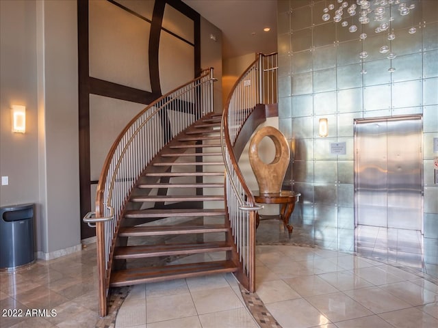 stairway with tile walls, tile patterned floors, elevator, and a high ceiling