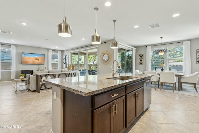 kitchen featuring pendant lighting, sink, dark brown cabinetry, light stone countertops, and a center island with sink