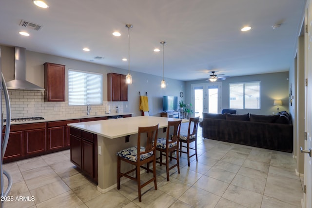 kitchen with french doors, wall chimney exhaust hood, decorative backsplash, a breakfast bar area, and stainless steel gas cooktop