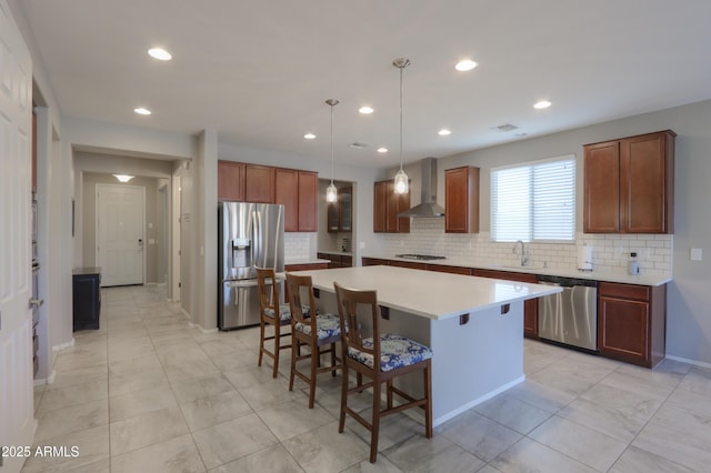 kitchen with a center island, wall chimney range hood, hanging light fixtures, sink, and appliances with stainless steel finishes