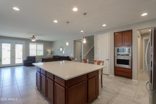 kitchen with ceiling fan, stainless steel appliances, a kitchen island, decorative light fixtures, and light tile patterned floors