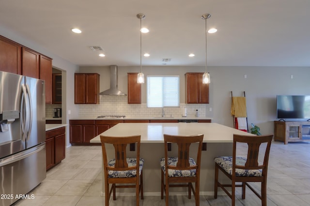 kitchen with wall chimney range hood, hanging light fixtures, decorative backsplash, appliances with stainless steel finishes, and a kitchen island