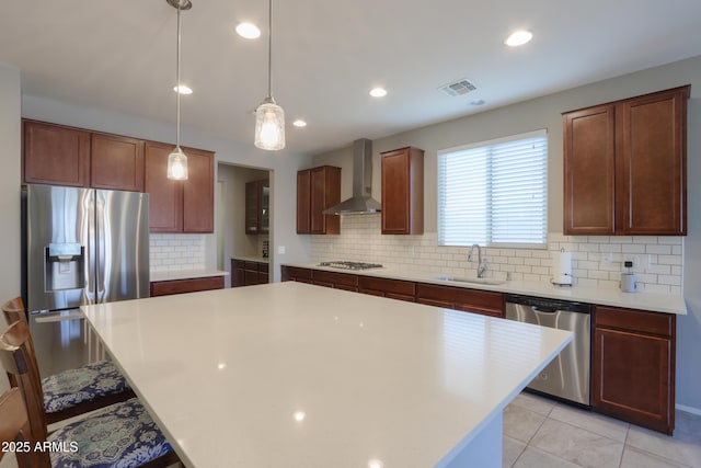 kitchen featuring a center island, sink, wall chimney exhaust hood, decorative light fixtures, and stainless steel appliances