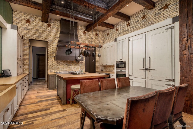 kitchen with light hardwood / wood-style flooring, brick wall, a high ceiling, and butcher block countertops