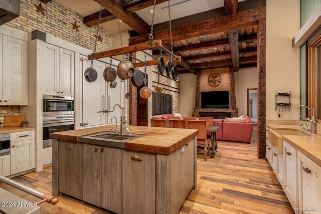 kitchen with sink, butcher block countertops, light hardwood / wood-style floors, beam ceiling, and a center island with sink