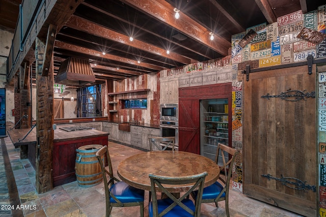 kitchen with beam ceiling, stainless steel appliances, a barn door, premium range hood, and wood walls