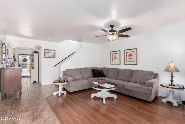 living room featuring a ceiling fan, arched walkways, stairs, and wood finished floors