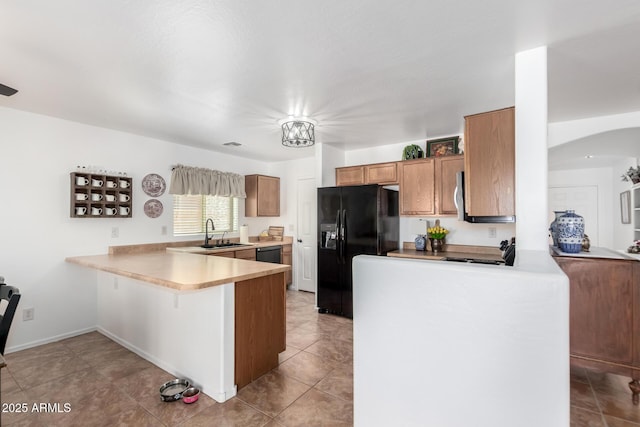 kitchen featuring light countertops, brown cabinets, a peninsula, and black appliances