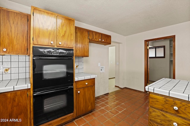 kitchen featuring decorative backsplash, a textured ceiling, black double oven, and tile counters