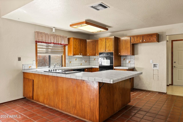 kitchen featuring tile counters, cooktop, dark tile patterned floors, kitchen peninsula, and decorative backsplash