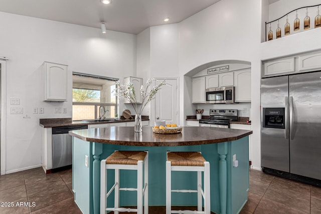 kitchen with a center island, a breakfast bar, a towering ceiling, white cabinetry, and appliances with stainless steel finishes