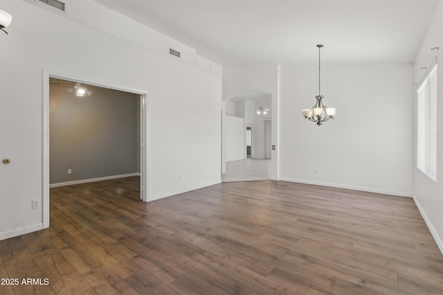 unfurnished living room featuring a chandelier, arched walkways, wood finished floors, and baseboards